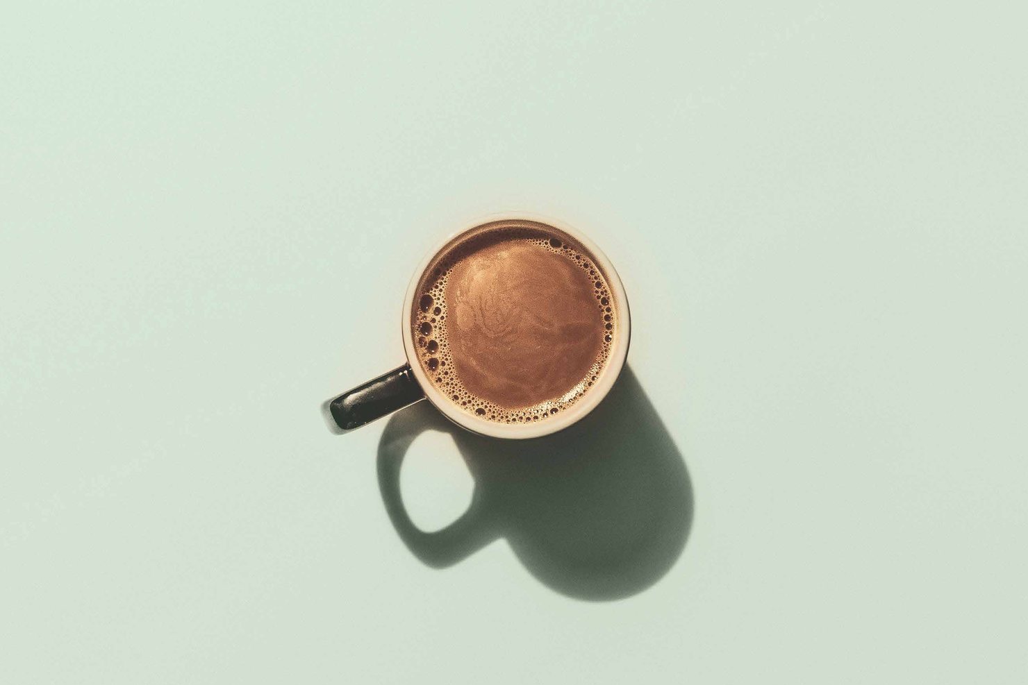 A cup of black coffee seen from above on a plain surface